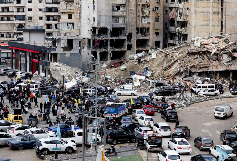 People gather as vehicles drive near damaged buildings, in Beirut's southern suburbs, after a ceasefire took effect. — Reuters