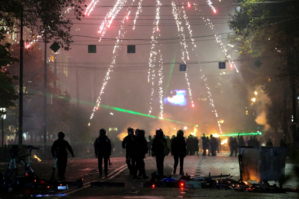 Law enforcement officers walk on a street as fireworks explode during a protest against the new government, in Tbilisi. — Reuters 