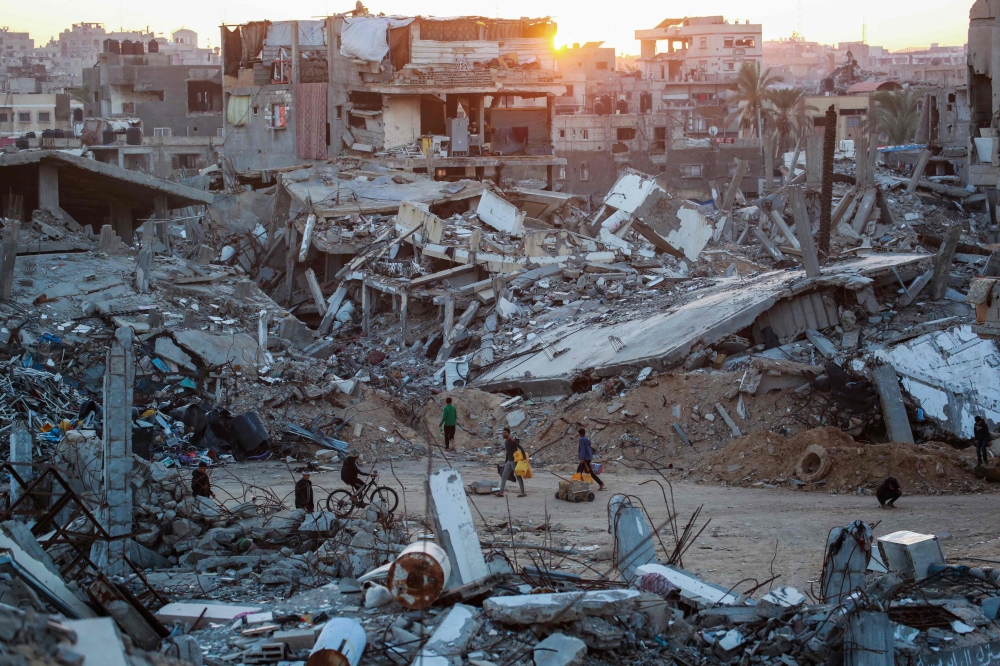  Palestinians walk in a devastated neighbourhood due to Israeli strikes in the southern Gaza Strip city. — AFP 
