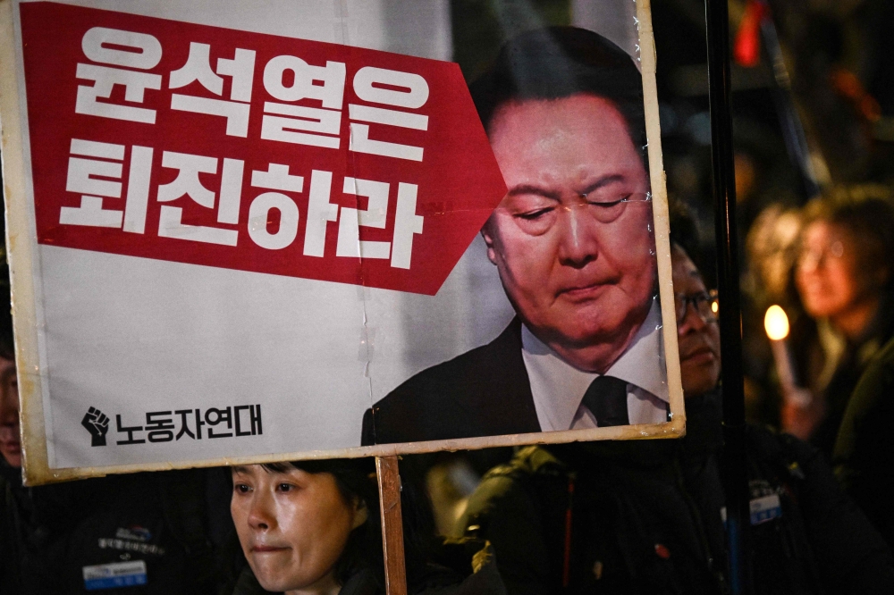 A woman holds a sign that reads "Yoon Suk Yeol should step down" during a candlelight vigil against South Korea President Yoon in Seoul on December 4, 2024. South Korea's opposition moved to impeach Yoon on December 4 after his extraordinary but short-lived imposition of martial law that brought thousands of protesters to the streets. (Photo by Philip FONG / AFP)