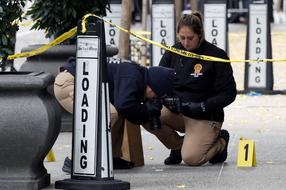 Members of the NYPD Crime Scene Unit work near evidence markers placed where shell casings were found at the scene where the CEO of UnitedHealthcare Brian Thompson was reportedly shot and killed in New York City. - Reuters

