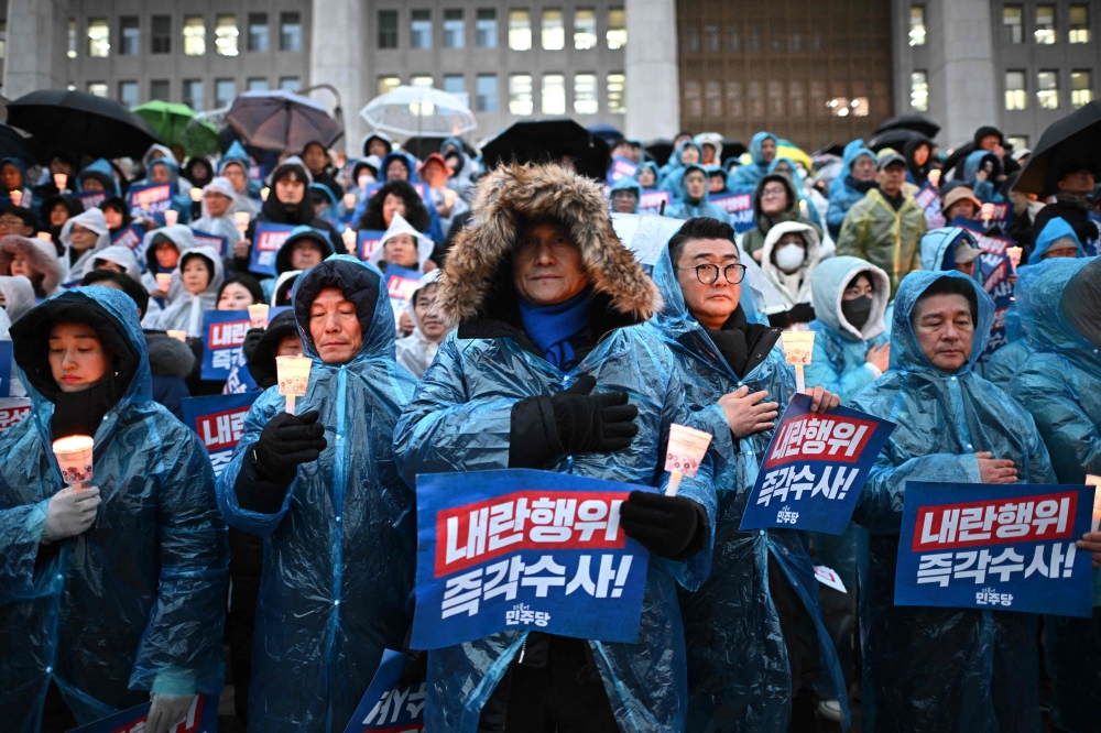 Protesters wear ponchos in the rain as they take part in a candlelight rally calling for the ouster of South Korea President Yoon Suk Yeol on the steps of the National Assembly in Seoul. - AFP