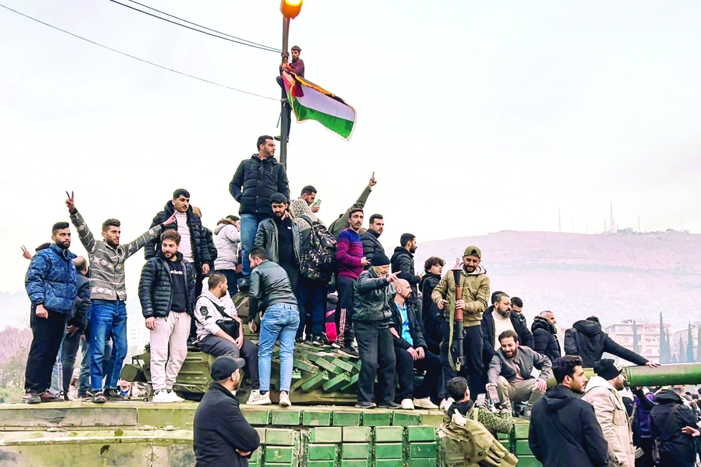 This screen grab shows people sitting on a tank as they gather at Umayyad Square in Damascus. — AFP 