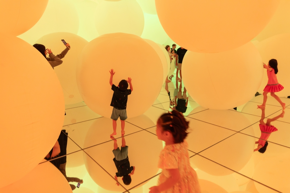Visitors in a room of giant orbs where colors change when they are touched at teamLab Planets in Tokyo, Oct. 4, 2024. (Shiho Fukada/The New York Times)
