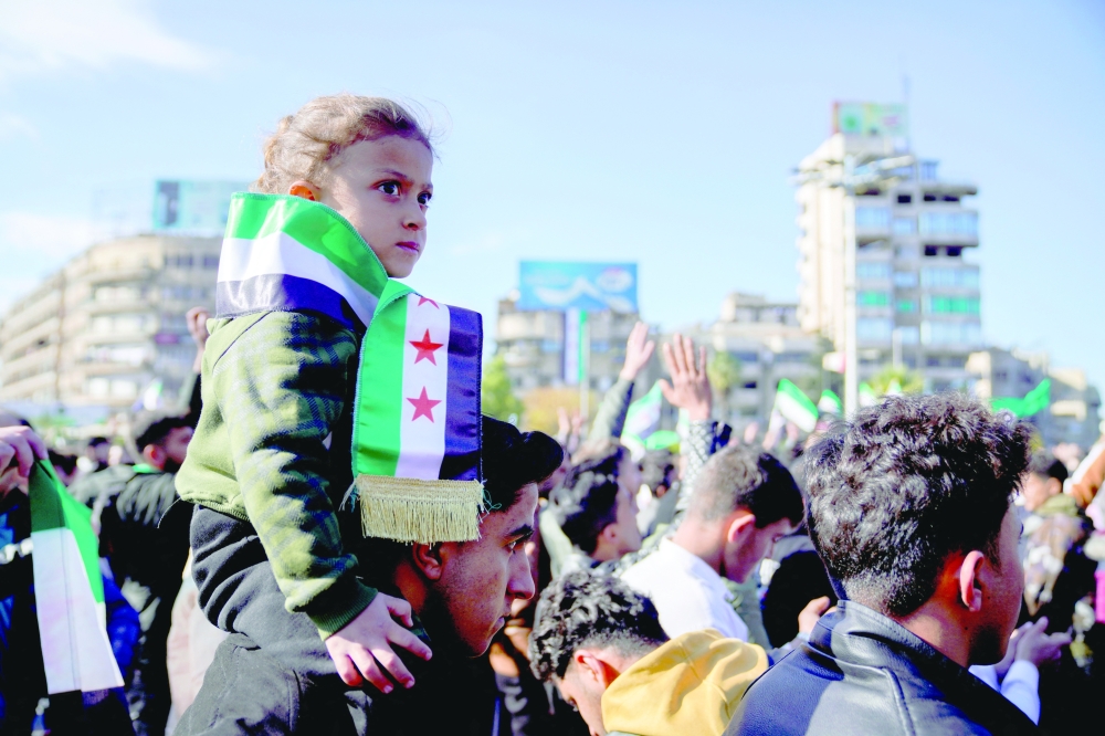 A man carries a child as people gather to celebrate, after fighters of the ruling Syrian body ousted Syria's Bashar al Assad in Aleppo. - Reuters