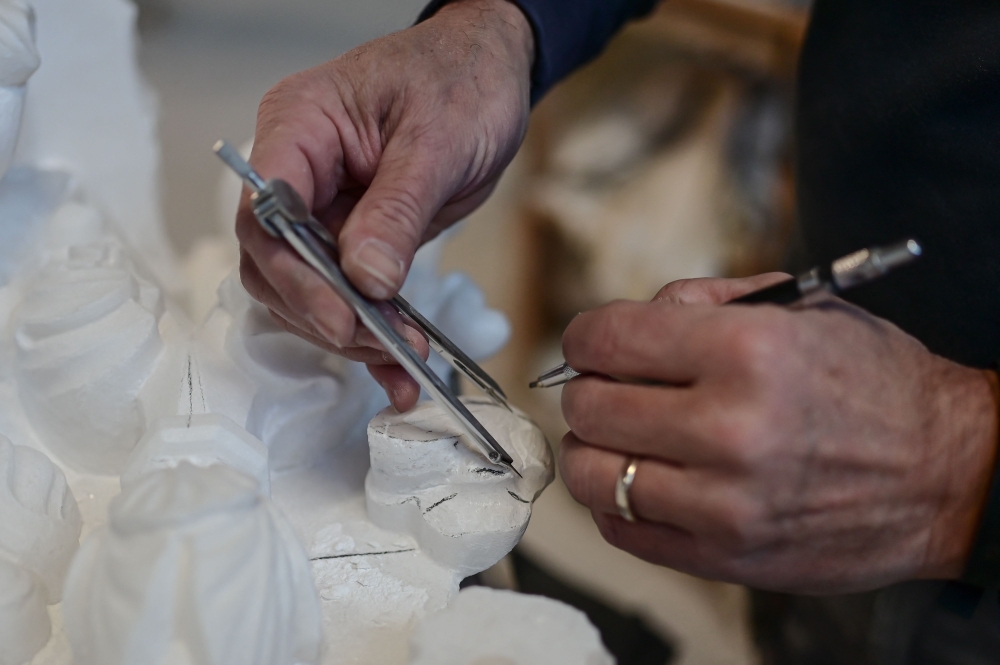 Ornamentalist Fabio Belloni, 55, marks the measures for carving on Candoglia marble spires of Milan's Duomo at the marble yard (Cantiere Marmisti) where blocks of marble are turned into ashlars, architectural and ornamental elements and statues on December 11, 2024 in Milan. Marble workers of the "Venerable Factory of the Duomo of Milan" (Fabbrica del Duomo) are taking care of more than 3.000 statues and gargoyles sculpted in marble from Candoglia quarries in the Italian Alps.  (Photo by Piero CRUCIATTI / AFP)

