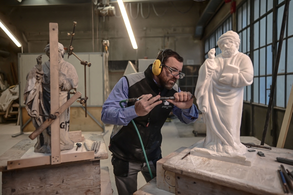 Sculptor Giovanni Calderino, 46, carves a Candoglia marble statue with a pneumatic hammer at Cantiere Marmisti, the marble yard where marble from the Candoglia quarry is turned into ashlars, architectural and ornamental elements,  sculptures and statues of Milan's Duomo Cathedral, on December 11, 2024 in Milan. On the left, a double-joint manual pantograph is visible, attached to the old marble statue to create precise copies through a pointing system. Marble workers of the "Venerable Factory of the Duomo of Milan" (Fabbrica del Duomo) are taking care of more than 3.000 statues and gargoyles sculpted in marble from Candoglia quarries in the Italian Alps.  (Photo by Piero CRUCIATTI / AFP)

