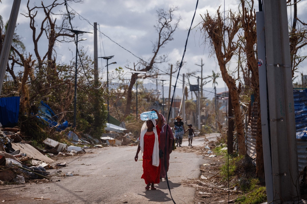 A woman carries water in Pamandzi, on the French Indian Ocean territory of Mayotte, after the cyclone Chido hit the archipelago. — AFP