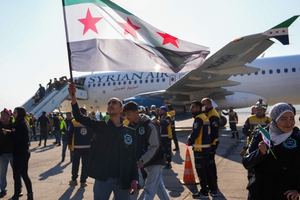A man lifts a Syrian flag as passengers disembark from a Syrian Air aircraft arriving from Damascus, at the airport of the northern city of Aleppo. — AFP 