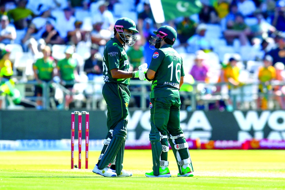Pakistan's Babar Azam (L) and Pakistan's Mohammad Rizwan (R) touch gloves as he congratulates his teammate for hitting a six during the second one day international (ODI) cricket match between South Africa and Pakistan at Newlands Cricket Ground in Cape Town on December 19, 2024. (Photo by Rodger Bosch / AFP)