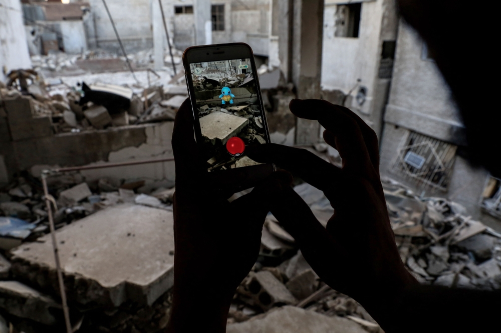 (FILES) A Syrian gamer uses the Pokemon Go application on his mobile to catch a Pokemon amidst the rubble in the besieged rebel-controlled town of Douma, a flashpoint east of the capital Damascus on July 23, 2016. With more than 60 million downloads and nearly 180 million dollars (171 million euros) generated worldwide since the end of October 2024, the mobile game adaptation of Pok駑on cards has enjoyed global success, not far from the records of its predecessor. 

