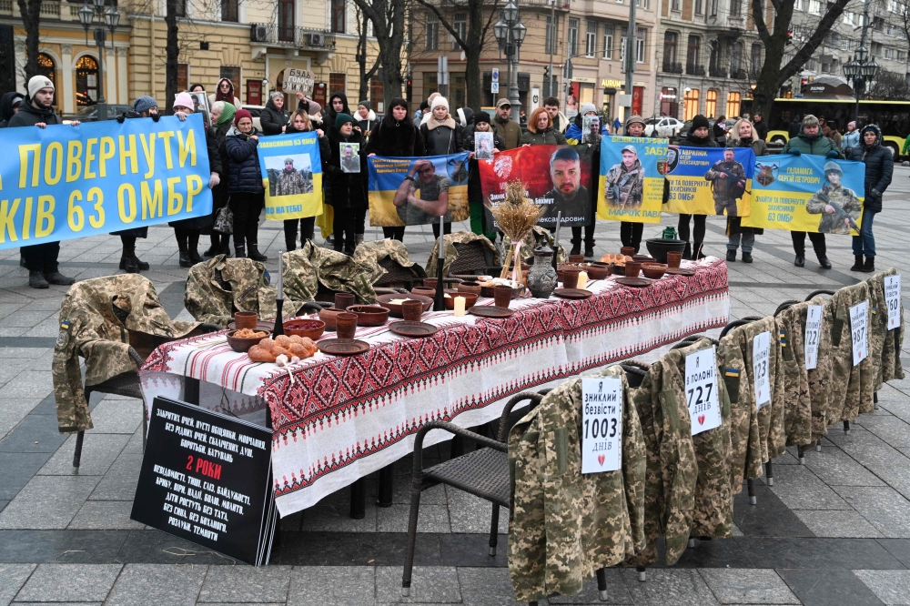 Soldiers' uniforms hang on empty chairs next to a symbolic Christmas table set with traditional dishes as people attend a rally in support of prisoners of war and missing soldiers in Lviv, Ukraine. — AFP 