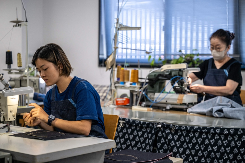 This picture taken on September 4, 2024 shows staff members working on denim fabric at the Momotaro Jeans factory in the Kojima district of Okayama. Call it an antidote to fast fashion: Japanese jeans hand-dyed with natural indigo and weaved on a clackety vintage loom, then sold at a premium to global denim connoisseurs. - To go with AFP story Japan-fashion-business-denim, FOCUS by Natuko Fukue

 (Photo by Philip FONG / AFP) / To go with AFP story Japan-fashion-business-denim, FOCUS by Natuko Fukue


