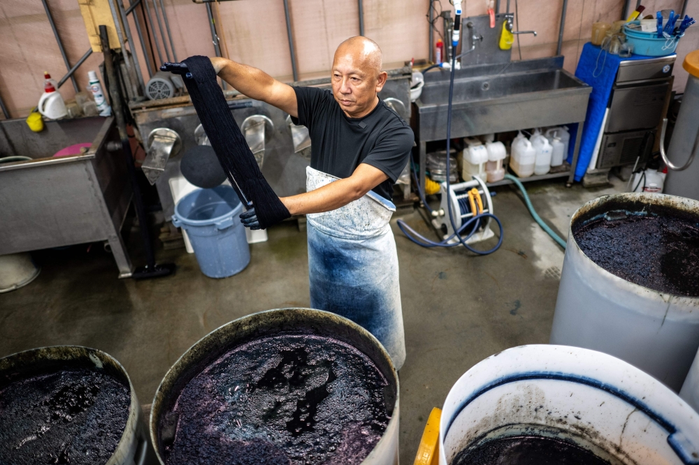 In this picture taken on September 4, 2024, dyeing craftsman Yoshiharu Okamoto demonstrates the hand-dyed fabrics process at the Momotaro Jeans factory in the Kojima district of Okayama. Call it an antidote to fast fashion: Japanese jeans hand-dyed with natural indigo and weaved on a clackety vintage loom, then sold at a premium to global denim connoisseurs. - To go with AFP story Japan-fashion-business-denim, FOCUS by Natuko Fukue

 (Photo by Philip FONG / AFP) / To go with AFP story Japan-fashion-business-denim, FOCUS by Natuko Fukue


