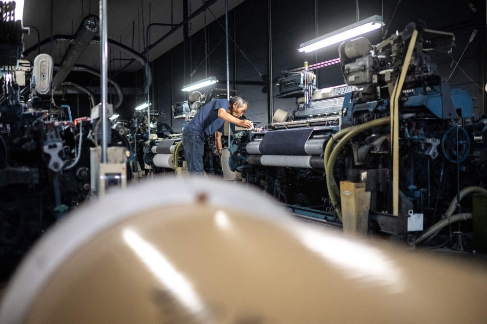 In this picture taken on September 4, 2024, weaving craftsman Shigeru Uchida checks looms for unusual sounds that could signal a breakdown at the Momotaro Jeans factory in the Kojima district of Okayama. Call it an antidote to fast fashion: Japanese jeans hand-dyed with natural indigo and weaved on a clackety vintage loom, then sold at a premium to global denim connoisseurs. - To go with AFP story Japan-fashion-business-denim, FOCUS by Natuko Fukue

 (Photo by Philip FONG / AFP) / To go with AFP story Japan-fashion-business-denim, FOCUS by Natuko Fukue


