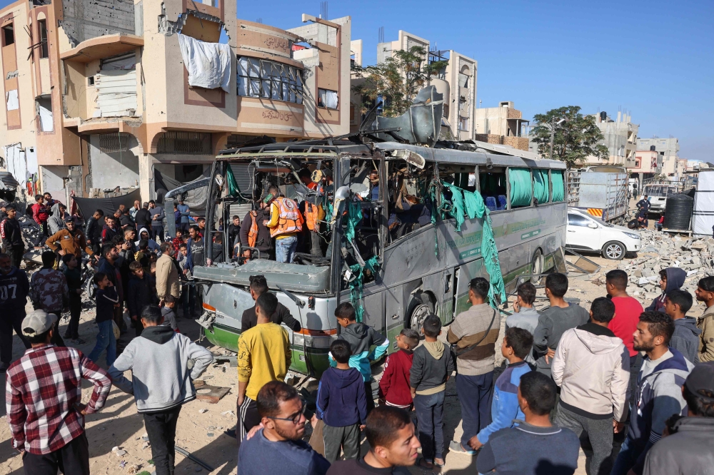People and rescuers inspect the carcass of a bus hit by an Israeli strike which led to casualties, in the Mawasi area. — AFP 