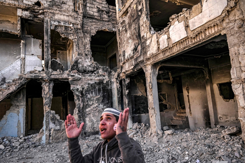Mahmud Khaled Ajaj reacts while standing before a destroyed apartment building in the Yarmuk camp for Palestinian refugees south of Damascus. - AFP

