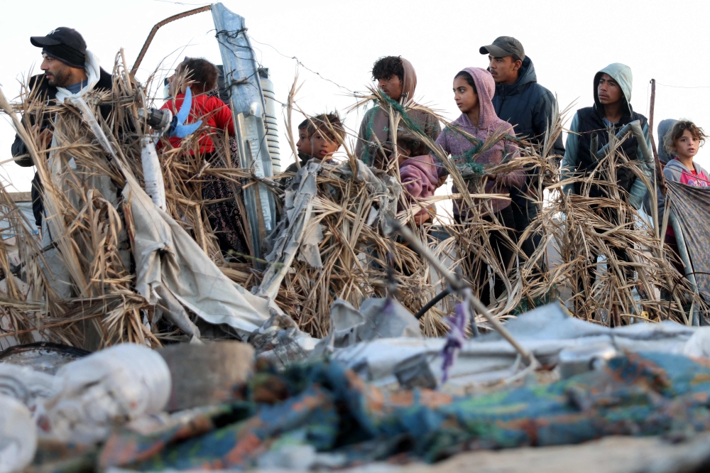 Men and children stand from afar to view the site of reported Israeli bombardment on tents sheltering Palestinians displaced from Beit Lahia at a camp in Khan Yunis. — AFP