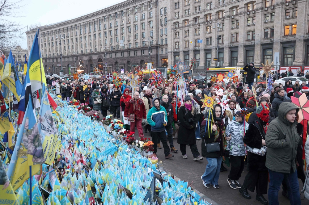 Ukrainians wearing traditional clothes pass by the makeshift memorial paying tribute to Ukrainian and foreign fighters during a Christmas procession at the Independence Square in Kyiv. — AFP 