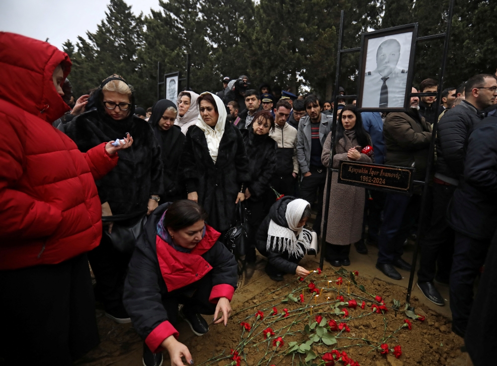 People mourn at the grave of Captain of the plane Igor Kshnyakin during the funeral, in Baku