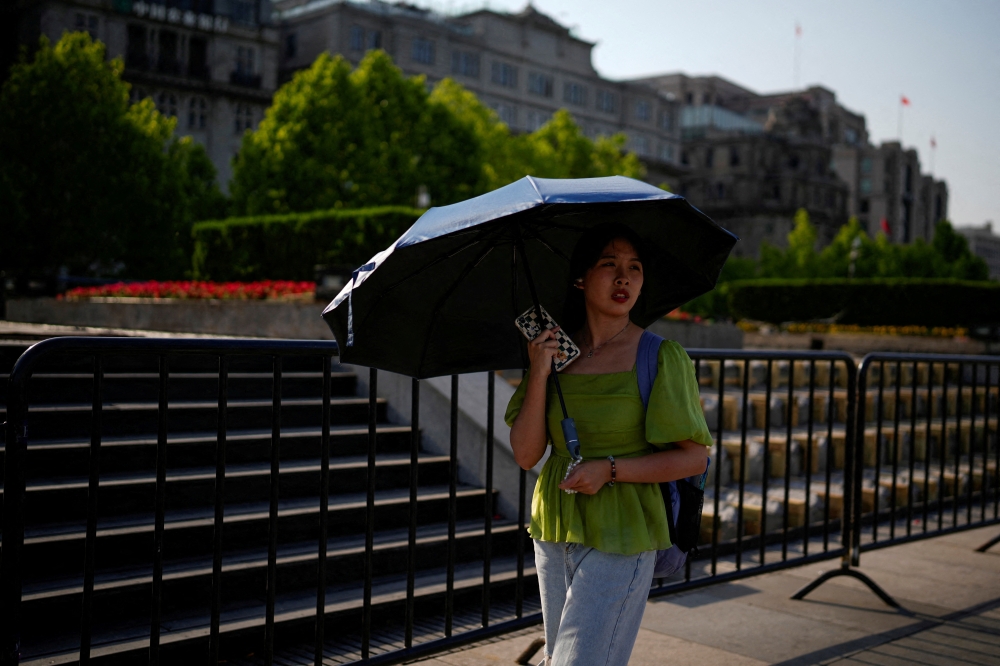 FILE PHOTO: A woman uses an umbrella to protect herself from the sun, as she walks on the Bund on a hot day, in Shanghai, China May 15, 2023. REUTERS/Aly Song/File Photo