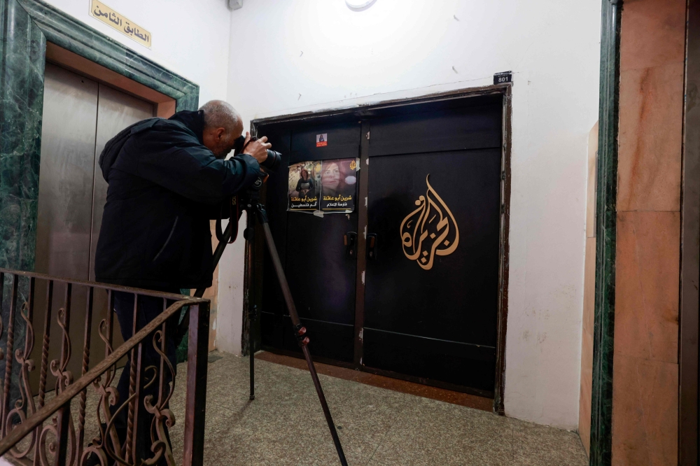 A man photographs the closed door of the Doha-based Al-Jazeera TV channel in the occupied-West Bank city of Ramallah on January 2, 2025. The Palestinian Authority has ordered the suspension of broadcasts by Al Jazeera across the Palestinian territories, accusing the network of incitement, official media reported. (Photo by Jaafar ASHTIYEH / AFP)

