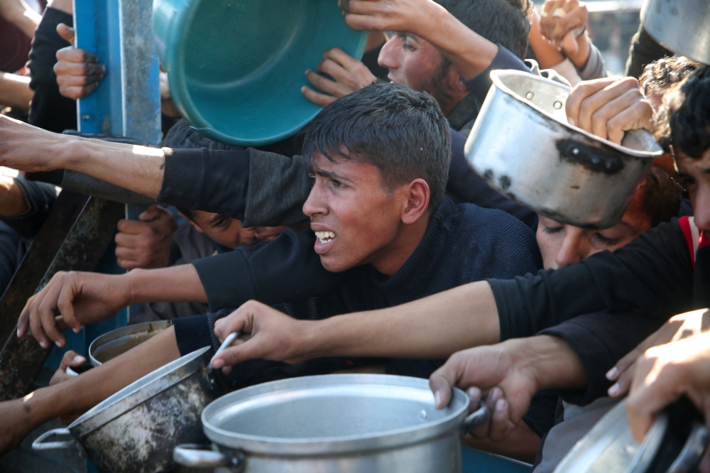 Palestinians gather to receive food cooked by a charity kitchen amid a hunger crisis in Khan Younis in the southern Gaza Strip. - Reuters