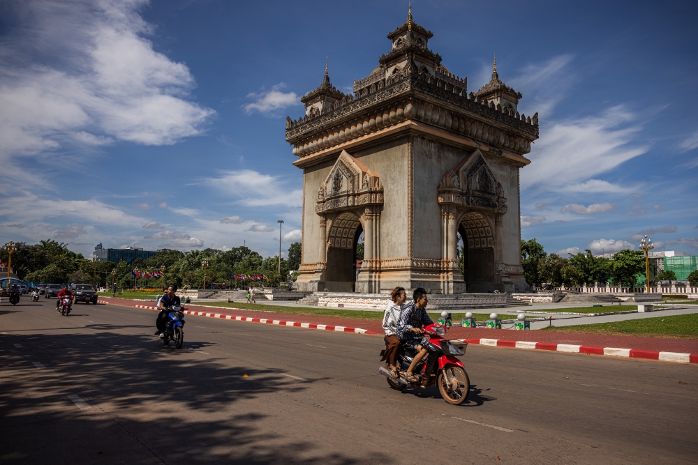 Locals drive past the Patuxay Monument, a war monument in downtown Vientiane, on October 20, 2024. (Lauren DeCicca/The New York Times)