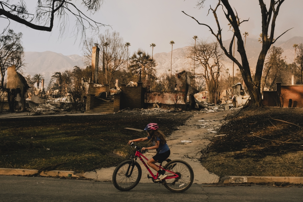 A young girl bicycles past the wreckage of homes destroyed by the Eaton Fire in Altadena, Calif., on Thursday, Jan. 9, 2025. (Mark Abramson/The New York Times)