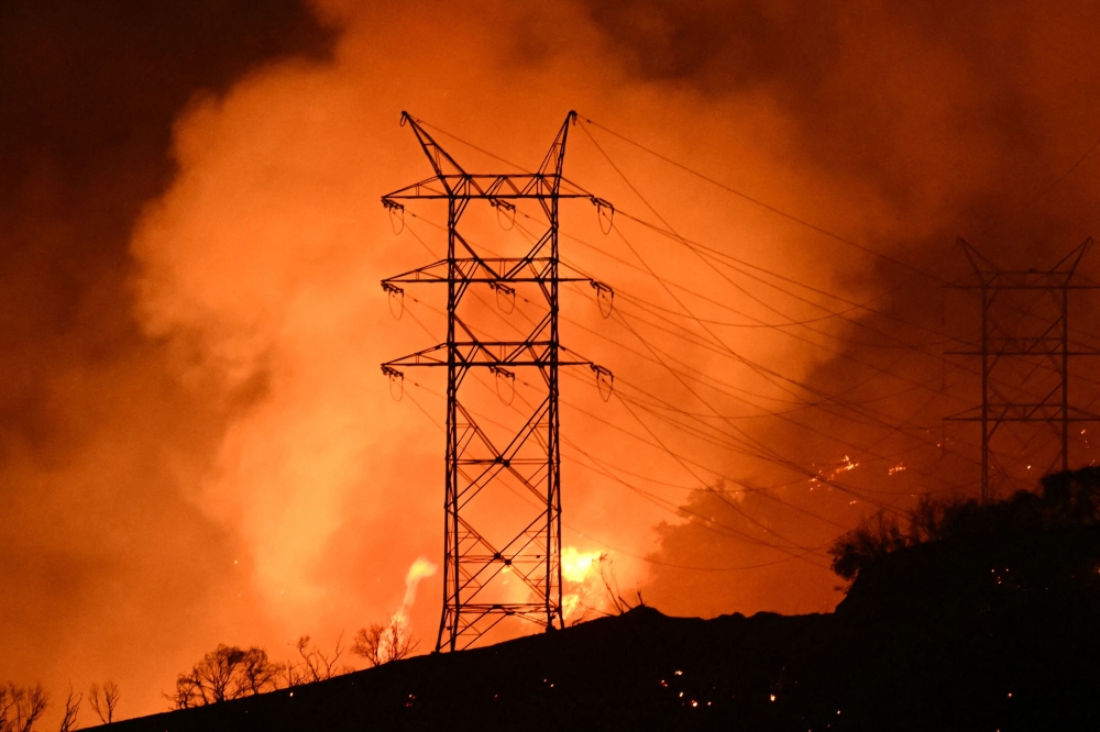 Flames and smoke are seen near power lines as the Palisades fire grows near the Mandeville Canyon neighborhood and Encino, California, on January 11, 2025. The Palisades Fire, the largest of the Los Angeles fires, spread toward previously untouched neighborhoods January 11, forcing new evacuations and dimming hopes that the disaster was coming under control. Across the city, at least 16 people have died as multiple fires have ripped through residential areas since January 7, razing thousands of homes in destruction that US President Joe Biden likened to a "war scene." (Photo by Patrick T. Fallon / AFP)

