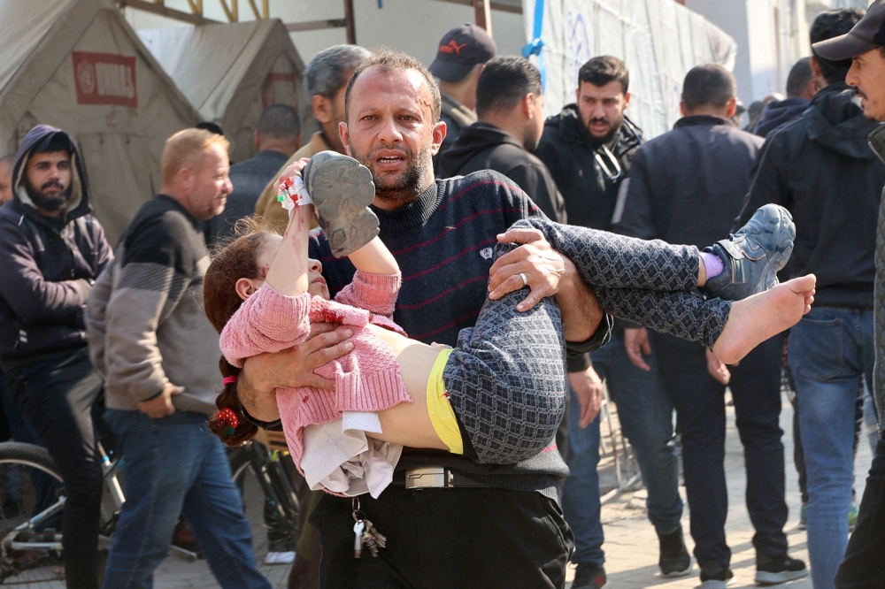 A Palestinian man carries a girl injured in Israeli strikes, into at Al-Ahli Arab hospital in Gaza City on Monday. - AFP