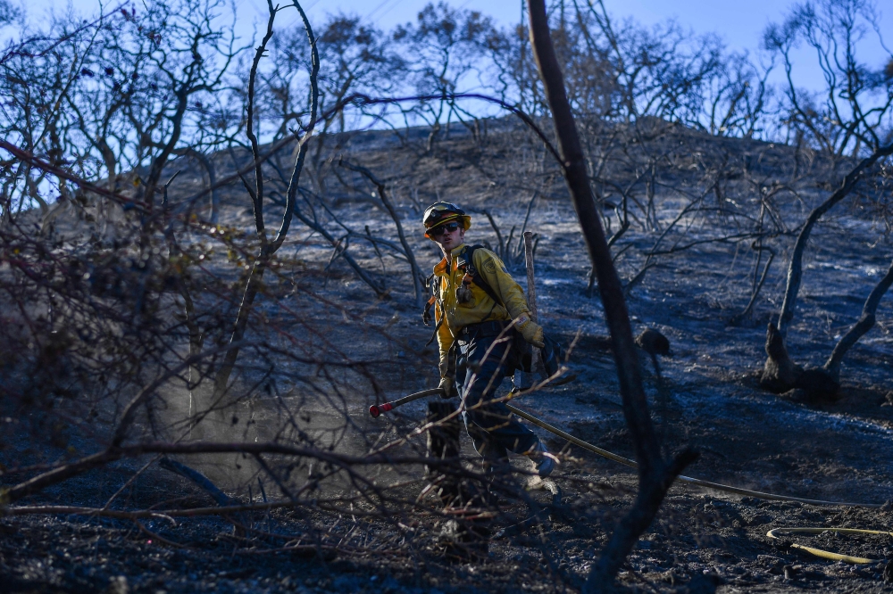 A firefighter works to extinguish the last embers in the hills of Mandeville Canyon, in Los Angeles. — AFP