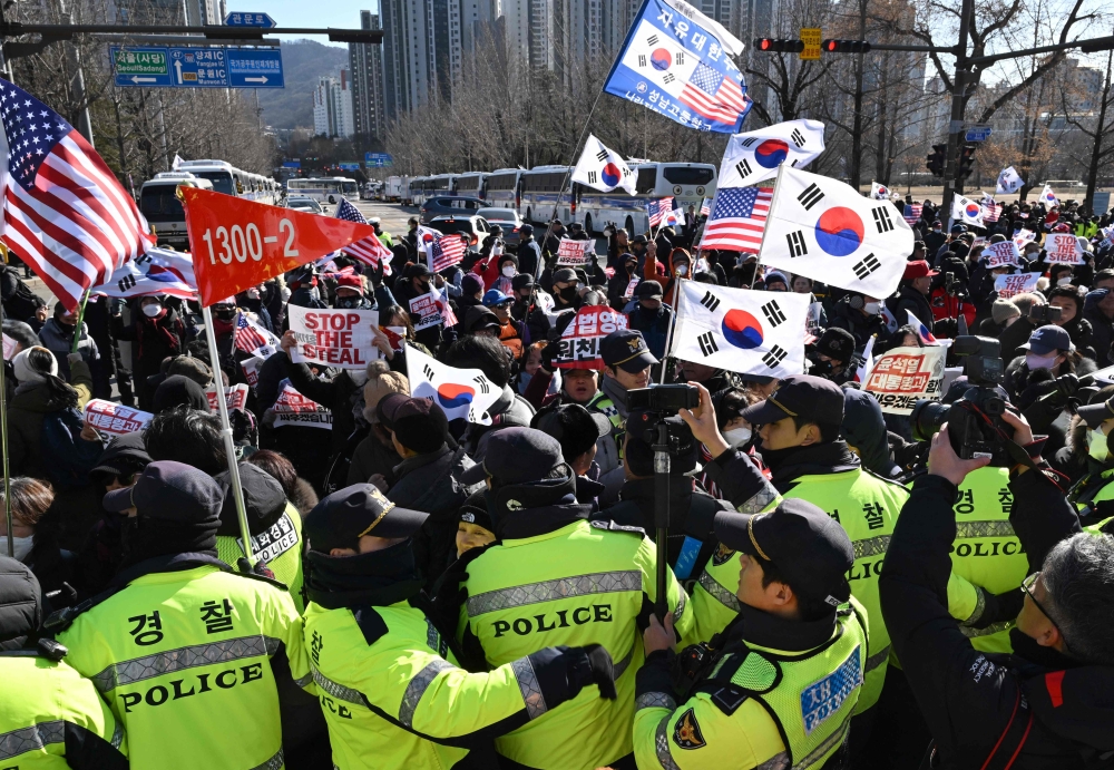 Supporters of impeached South Korean president Yoon Suk Yeol wave South Korea and the US flags as they gather outside  the Corruption Investigation Office, in Gwacheon