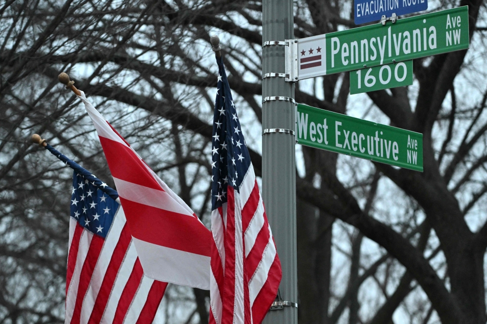 The flag of the District of Columbia (C) and US flag are set up outside the White House in Washington, DC. — AFP 