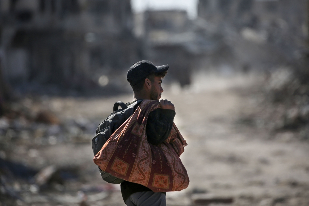 A Palestinian youth carrying his belongings walks amidst building rubble in a ruined neighbourhood of Rafah on Monday. - AFP