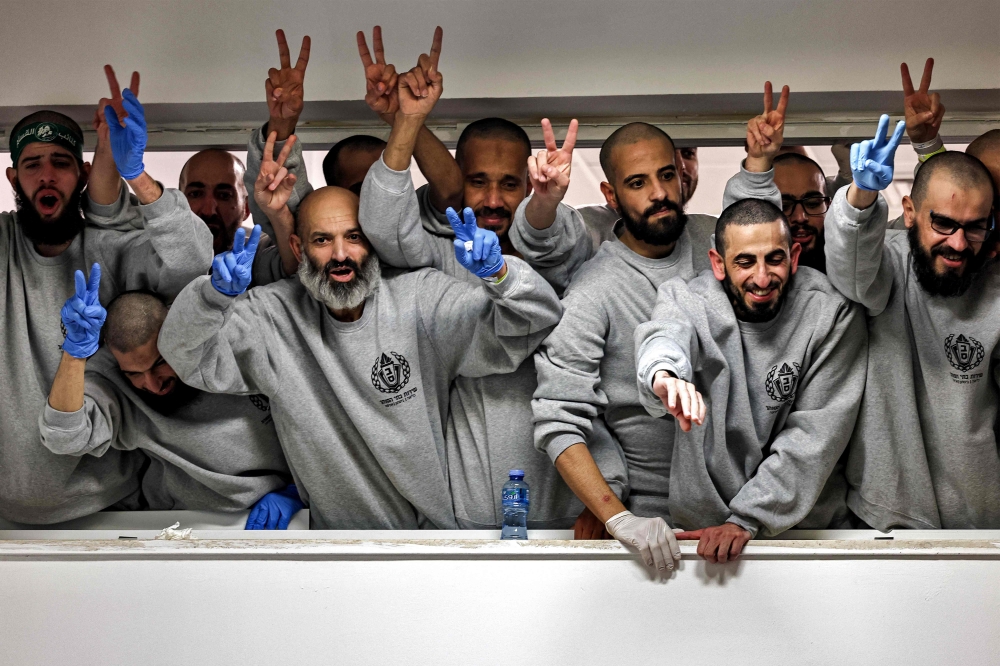 Palestinian prisoners released by Israel wave and cheer to people below gathering to receive them at a sports centre building of the Ramallah municipality on Saturday. - AFP