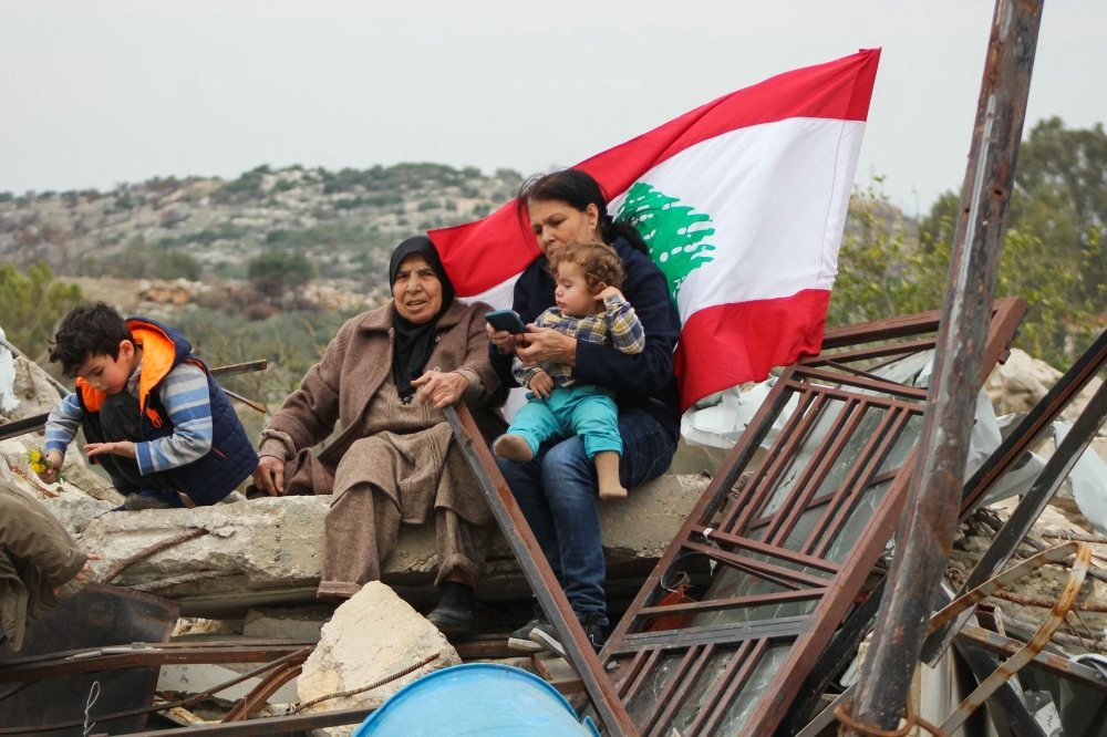Displaced residents lift a Lebanese flag as they sit on the rubble of their home in their southern Lebanese village of Yarin. — AFP 