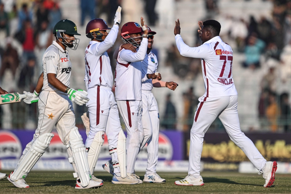 West Indies' Kevin Sinclair (R) celebrates with his teammates after taking the wicket of Pakistan's Babar Azam (L) during the second day of the second Test cricket match between Pakistan and West Indies at the Multan Cricket Stadium in Multan on January 26, 2025. (Photo by Farooq NAEEM / AFP)

