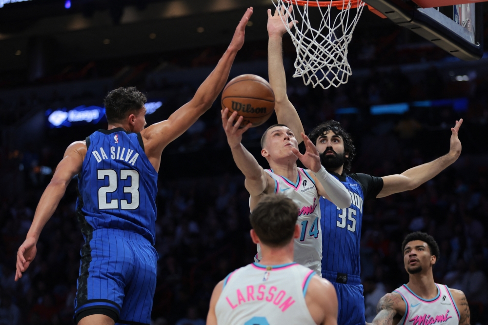 Jan 27, 2025; Miami, Florida, USA; Miami Heat guard Tyler Herro (14) scores past Orlando Magic forward Tristan da Silva (23) and center Goga Bitadze (35) during the second quarter at Kaseya Center. Mandatory Credit: Sam Navarro-Imagn Images
