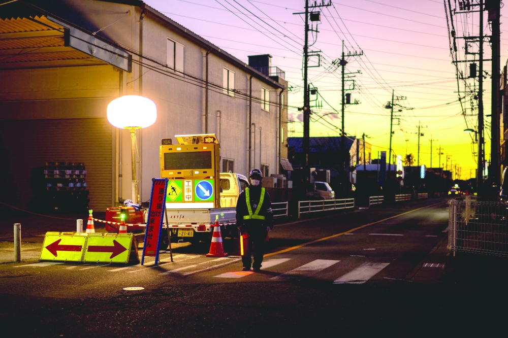 A worker controls the traffic as rescue operations continue for a truck driver after his vehicle plunged into a sinkhole in Yashio. — AFP 
