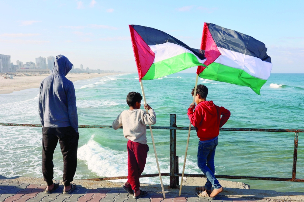 Two boys standing by a coastal area hold Palestinian flags in Gaza City. — AFP 