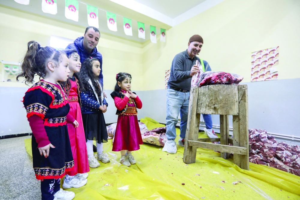 Children dressed in traditional outfits watch as men prepare portions of meat as part of Algeria's Tamechrit, based on the Amazigh New Year's traditions, in Bajaia, on January 11, 2025. Algerian villages are perpetuating, particularly in Kabylia, the centuries-old tradition of Tamechrit, based on mutual aid and suspended during the civil war of the 1990s. (Photo by AFP)