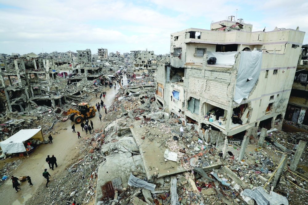 Palestinians walk past the rubble of buildings destroyed during the Israeli offensive on a rainy day in Gaza City. - Reuters