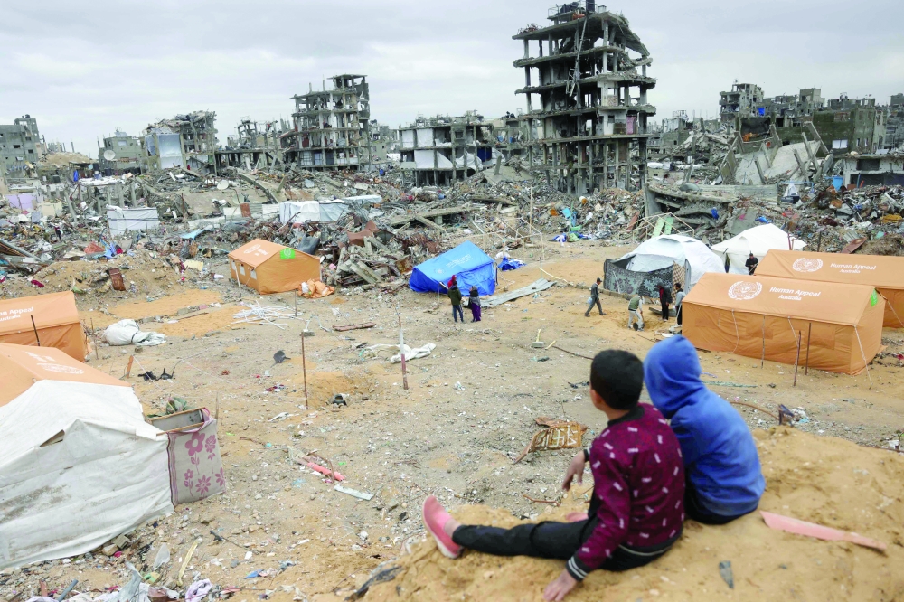 Children sit on a sand mound overlooking tents set up amid destroyed buildings in Jabalia in the northern Gaza Strip on Thursday. — AFP