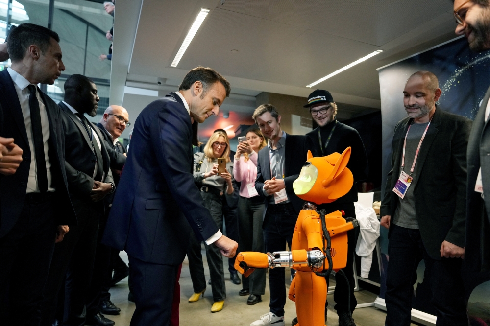 French President Emmanuel Macron bumps fists with a robot during a visit to Station F, as part of an event on the sidelines of the Artificial Intelligence Action Summit in Paris, on Tuesday. - Reuters