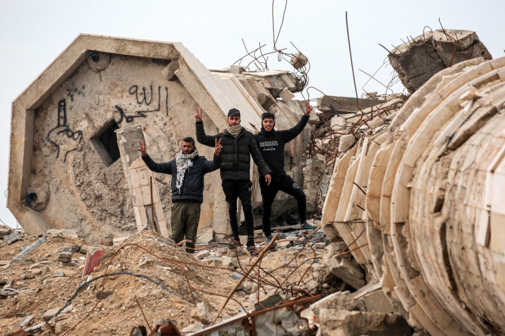 TOPSHOT - Men gesture as they stand by the remains of a collapsed building in the west of Beit Lahia in the northern Gaza Strip on February 11, 2025 amid the current ceasefire deal in the war between Israel and Hamas.  (Photo by BASHAR TALEB / AFP)
