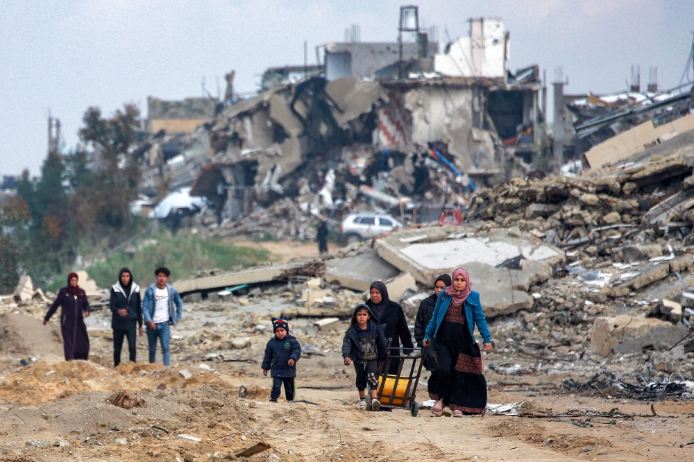 Women and children walk along a destroyed road past collapsed buildings in the west of Beit Lahia in the northern Gaza Strip.— AFP