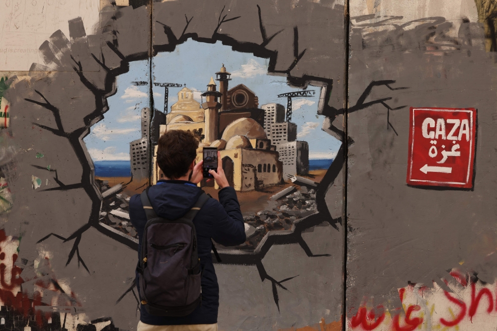 A man takes a picture of graffiti representing the reconstruction of Gaza, on a section of Israel's separation barrier, in Bethlehem in the occupied West Bank on Wednesday. - AFP