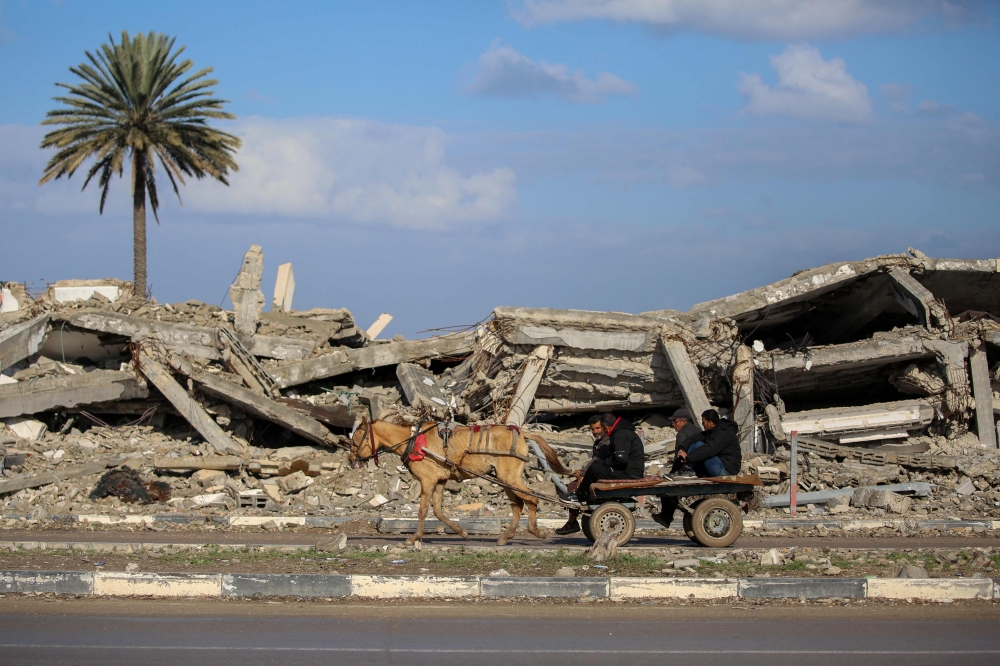 Civilians ride an animal pulled cart past the rubble of a destroyed building in Al Mughraqa in the central Gaza Strip, as displaced people move towards the northern parts of Gaza during a current ceasefire deal between Israel and Hamas. - AFP

