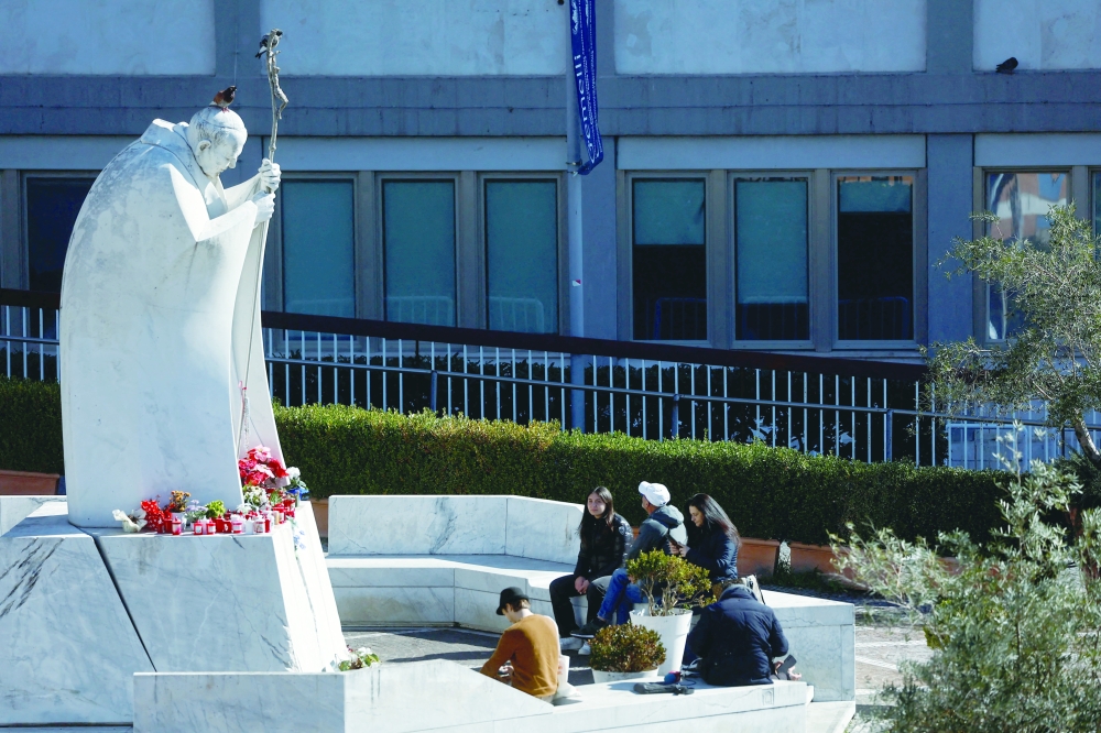 People sit next to the statue of late Pope John Paul II outside the Gemelli Hospital, in Rome. — Reuters